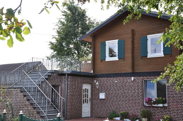 A two-story brick house with a wooden facade, a metal staircase, and a small balcony.