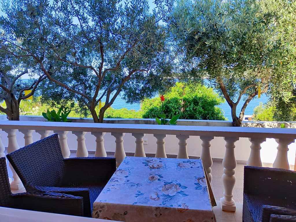 Un balcon agrémenté de chaises et d’une table en osier, offrant une vue panoramique sur un paysage arboré et un plan d’eau.