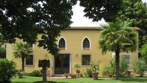 Un bâtiment jaune avec un jardin devant. On y trouve des plantes en pot et un palmier.