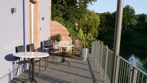 An outdoor patio with a table and chairs, a potted plant, and a view of a river.