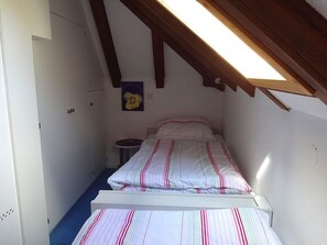 Ein kleines Zimmer mit einem Einzelbett, geneigter Decke und einem Oberlicht.