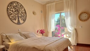 A bedroom with a bed, a nightstand, a wall-mounted tree decoration, a window with sheer curtains, and a view of the outside. - Oasis of peace in the Algarve, private pool, heating (Sao Bras de Alportel)