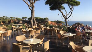 An outdoor dining area with wicker furniture and tables, overlooking a coastal landscape with trees and cliffs. - Oasis of peace in the Algarve, private pool, heating (Sao Bras de Alportel)