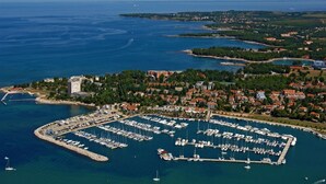 An aerial view of a coastal town with a marina filled with boats, surrounded by residential buildings and greenery.
