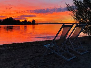 A sunset over a calm lake with a chair by the water's edge. - Ferienwohnung "Genusszeit am Chiemsee" EG mit Terrasse (Übersee)