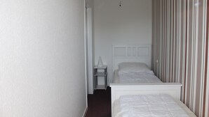 Habitació estreta amb dos llits individuals, una petita taula de nit blanca i una làmpada blanca.