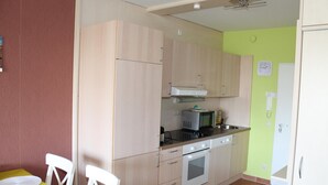 Una cuina compacta amb armaris de fusta clara, microones, forn i rentapeus. Hi ha una taula de dinar amb cadires i una catifa al sòl.