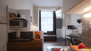 Cocina compacta con microondas, cafetera y comedor con mesa y sillas.