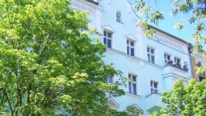 Un edificio de varios pisos con fachada azul claro, ventanas amplias y un árbol en primer plano.