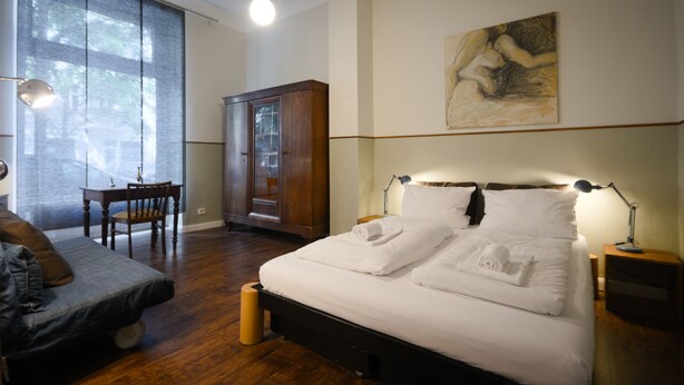 Un dormitorio con una cama, un armario de madera, un escritorio con silla y un ventanal grande.