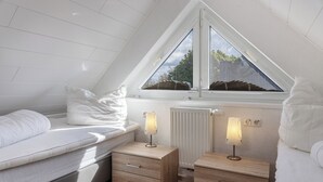Een slaapkamer met een schuine kap, een bed met witte lakens, twee nachtkastjes met lampen en een radiator.