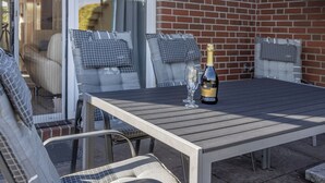 Een terras buiten met een tafel, stoelen en een fles champagne.