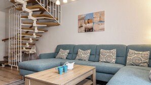 Een woonkamer met een blauwe bank, een houten salontafel en een spiltrap.