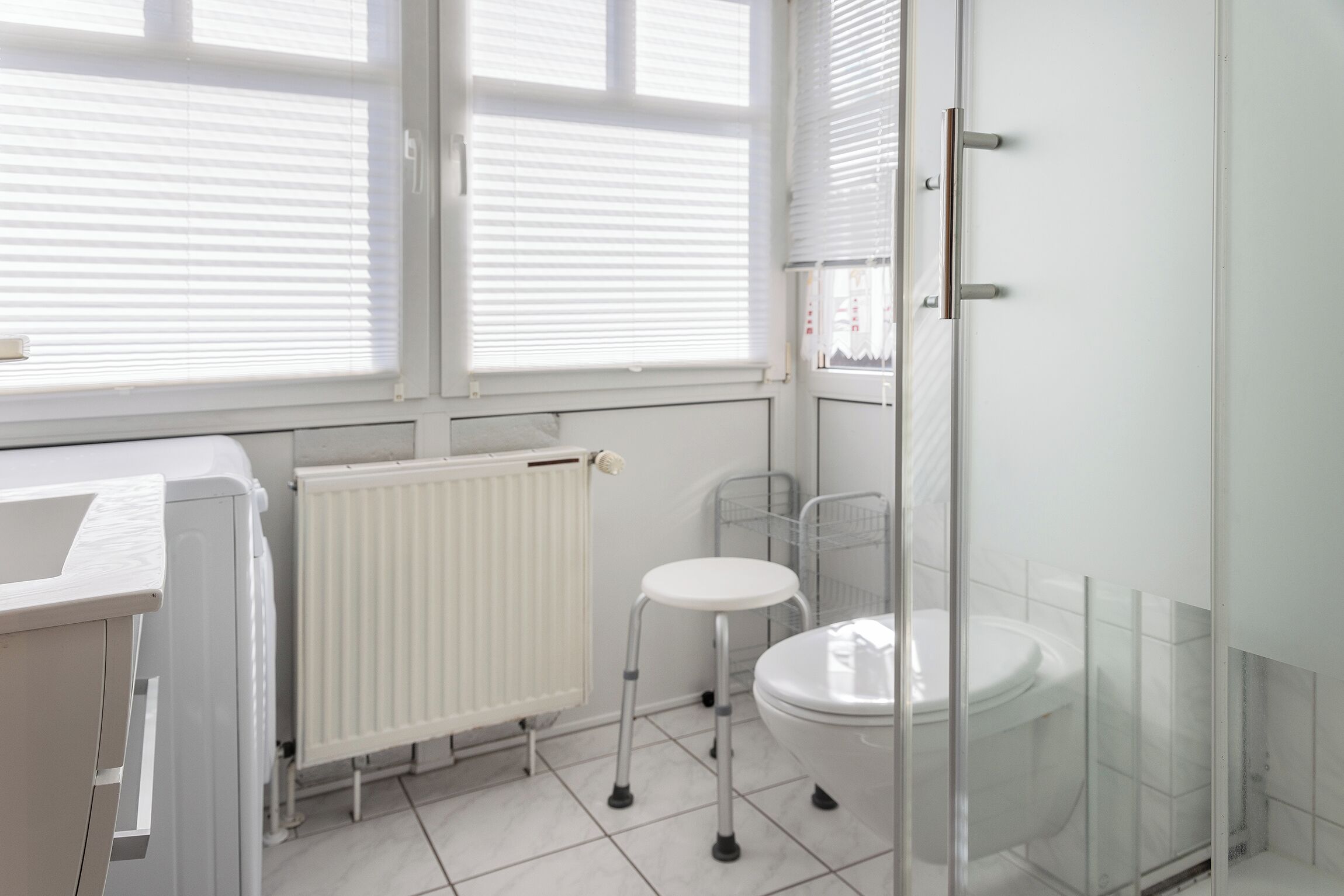 A bathroom with a toilet, a radiator, a window with blinds, and a shower area.