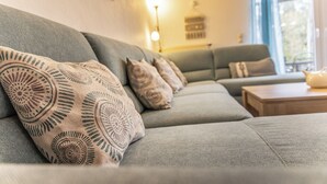 Een moderne woonkamer met een grijze bank, decoratieve kussens met een patroon, een houten salontafel en een vloerlamp.