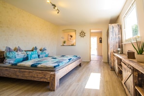 Ein Schlafzimmer mit einem Holzbett, einer Holzkommode, einer Topfpflanze und einem Fenster.