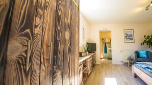 A modern living room with a wooden cabinet, a television, a sofa, and a plant. - 30sqm vacation apartment close to the beach in the countryside (Stubbenfelde)