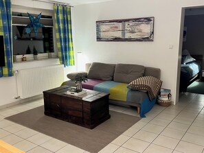 Een woonkamer met een bank, een salontafel, een radiator en een raam met gordijnen.