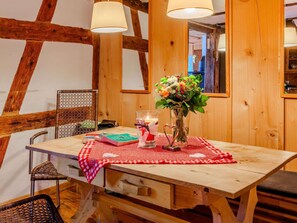 A wooden dining table with a red and white checkered tablecloth, a vase of flowers, a candle, and books. - Historic Gerberhaus - Romantic with Sauna, fireplace, handmade furniture, wifi (Alpirsbach)