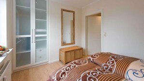 A bedroom with a wardrobe, a mirror, a bedside table, and a bed with patterned bedding. - High quality apartment, Büsum, W-Lan, 200m to the beach, 300m to the center, promenade (Büsum)
