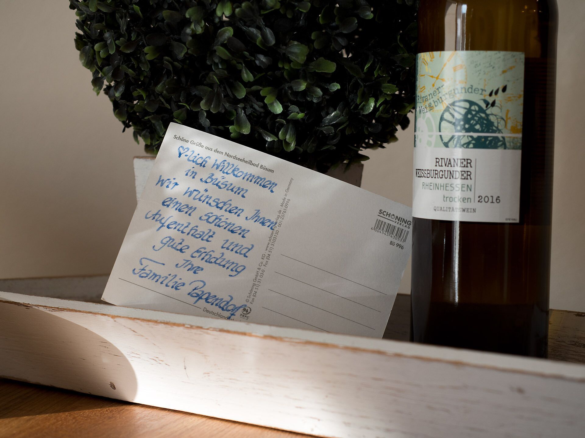 A bottle of wine with a label and a handwritten note on a wooden surface.