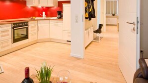 A modern kitchen with white cabinets, a red accent wall, and a dining area with a red rug, wine glasses, and a book. - High quality apartment, Büsum, W-Lan, 200m to the beach, 300m to the center, promenade (Büsum)