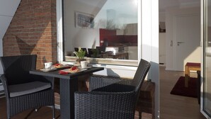 A dining area with wicker chairs and a table, a sliding glass door leading to a kitchen, and a red rug on the floor. - High quality apartment, Büsum, W-Lan, 200m to the beach, 300m to the center, promenade (Büsum)
