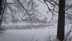 Lumipeitteinen maisema, jossa on paljaita puita ja kauempana näkyvä rakennus.