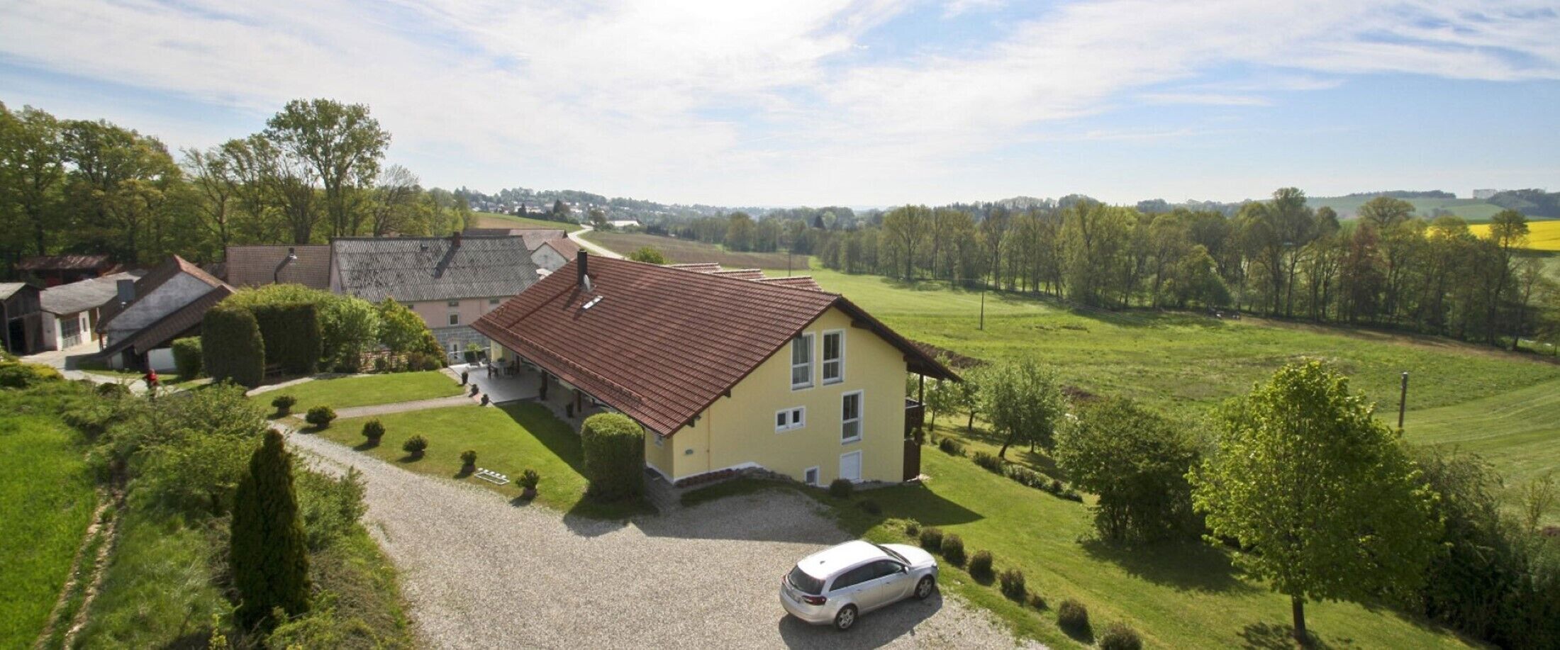 Une maison avec un toit rouge, entourée d’une pelouse bien entretenue et d’une allée gravillonnée.