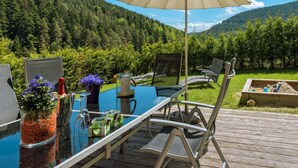Un espace extérieur aménagé pour les repas, avec une table en verre, des chaises et un parasol.