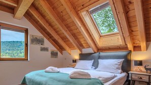 Une chambre avec un plafond en pente, un puits de lumière, un lit recouvert de draps blancs et une vue sur une forêt par la fenêtre.