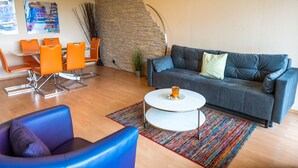 A lounge area with a stone accent wall, a grey sofa, orange chairs, and a colorful rug.