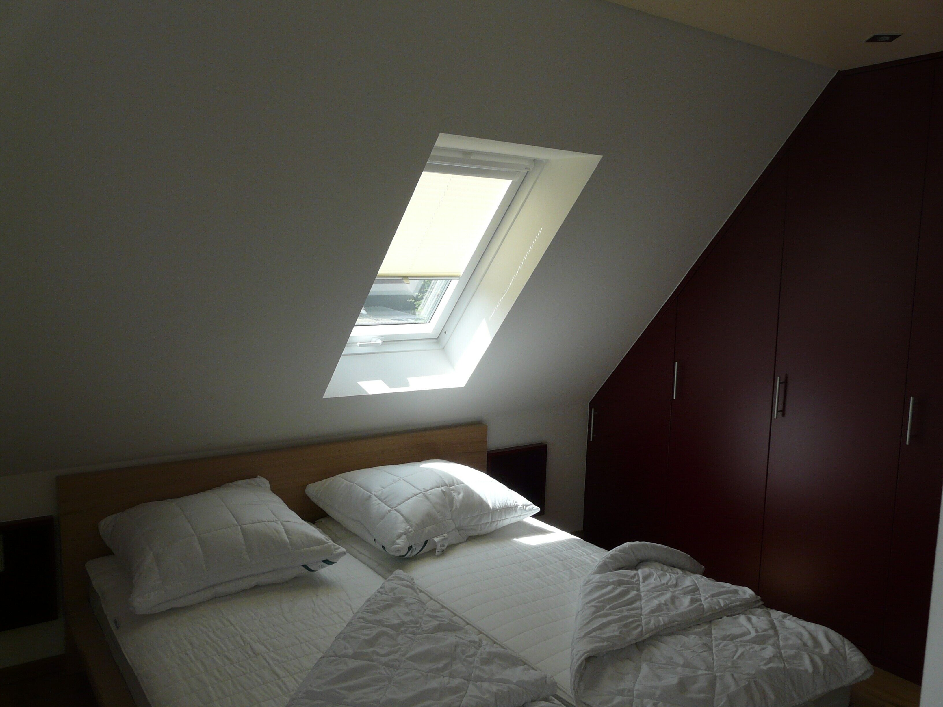 Une chambre avec un plafond en pente, un puits de lumière et un lit recouvert de linge de lit blanc.