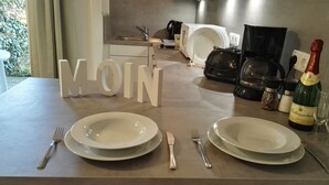 Een eettafel gedekt met borden, bestek en een fles champagne. Opvallend grote letters vormen het woord 
