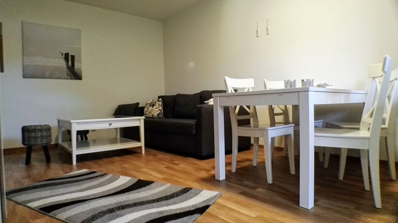 Una sala de estar con un sofá, una mesa de comedor con sillas, una mesita auxiliar y una alfombra.