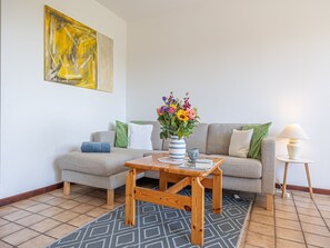 A living room with a sofa, a coffee table, a vase with flowers, a lamp, and a painting on the wall.