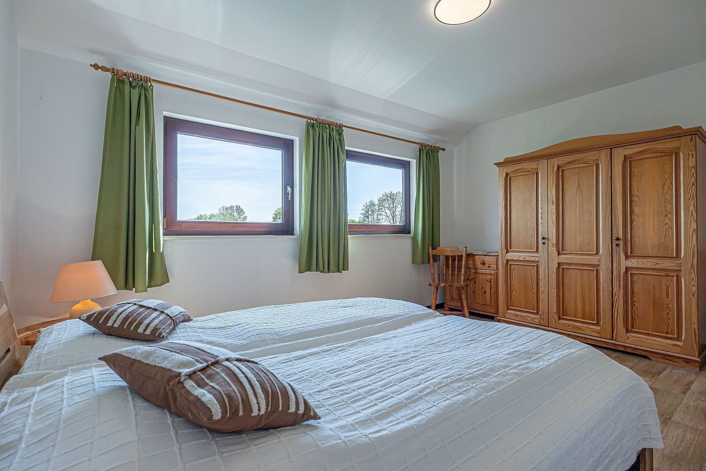 Een slaapkamer met twee bedden, groene gordijnen, een houten kledingkast en een raam met uitzicht.