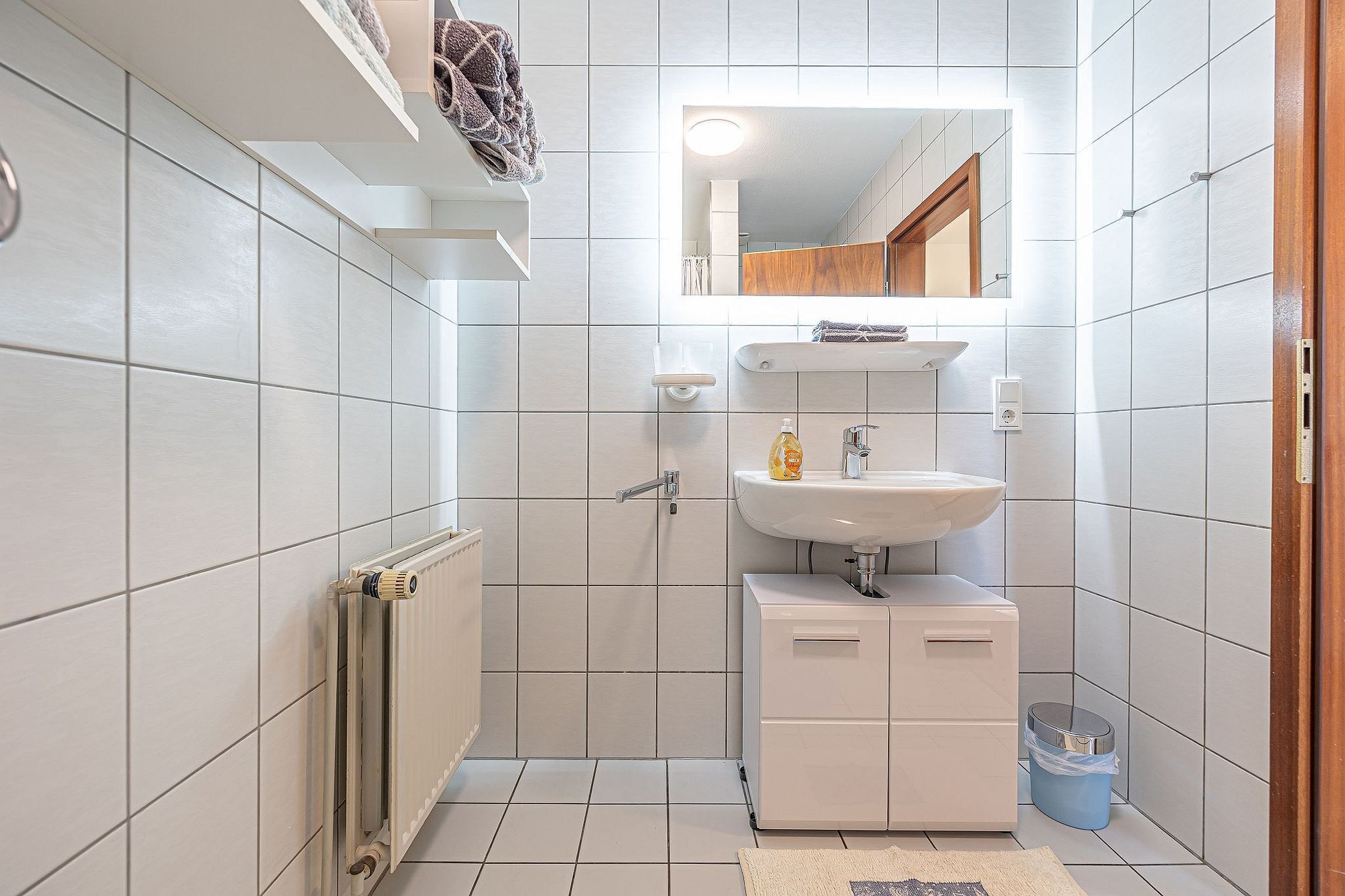 A small bathroom with white tiles, a white sink, a mirror, and a towel rack.