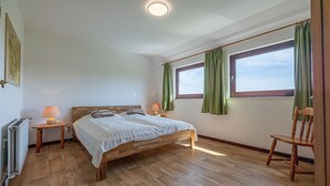 Una camera da letto con un letto di legno, un comodino con una lampada, una sedia e una finestra con tende.