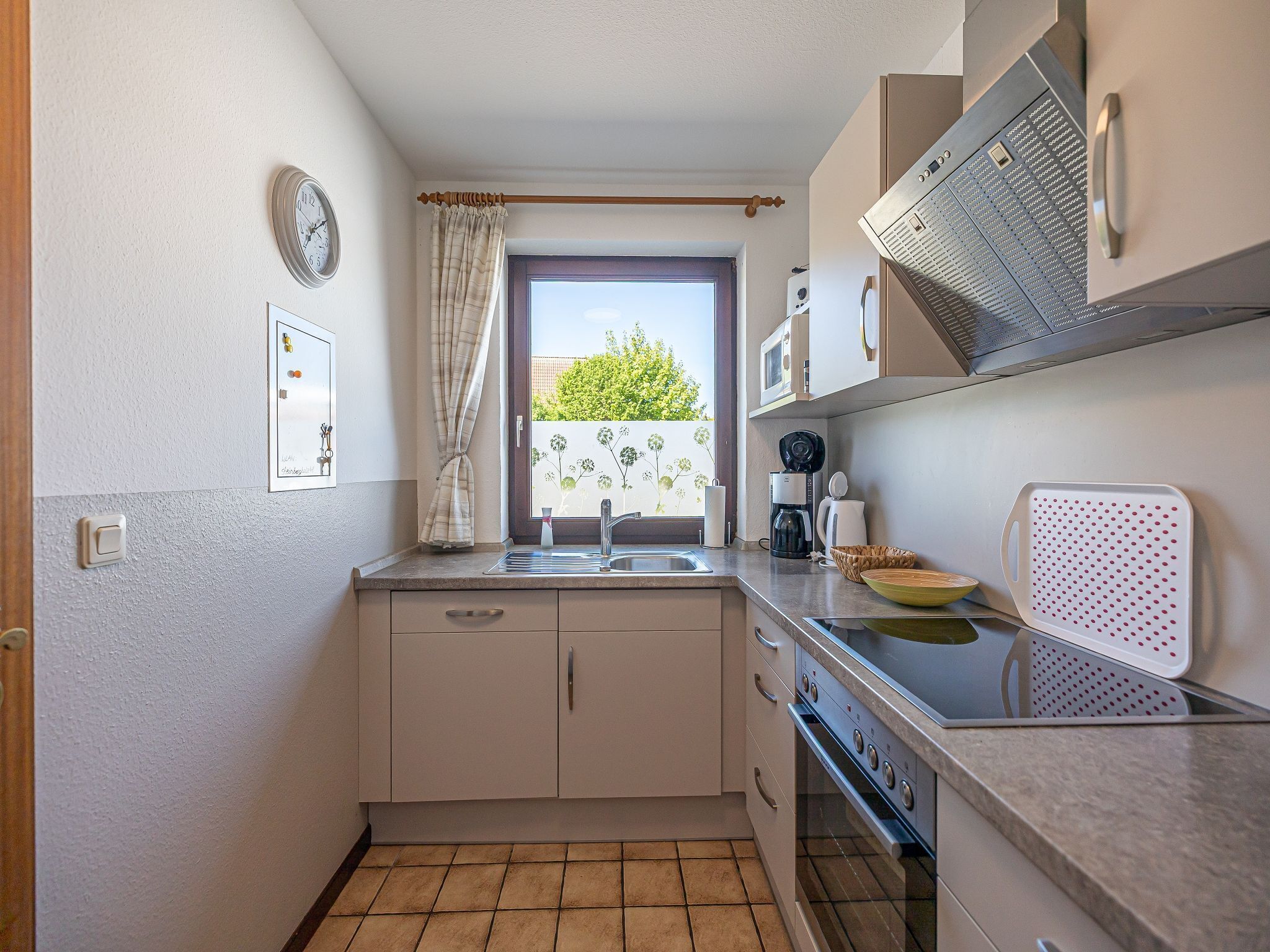 A compact kitchen with a window, a clock, a microwave, and a coffee maker.