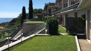 A modern residential building with a stone facade, a balcony with metal railings, and a view of the sea. - Design apartment - 100 sqm green terrace - Pool - Fantastic panoramic lake view (Toscolano-Maderno)