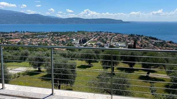 A coastal town with a view of the sea and mountains in the distance. - Design apartment - 100 sqm green terrace - Pool - Fantastic panoramic lake view (Toscolano-Maderno)