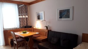 A cozy living room with a wooden dining table, a black sofa, and a window with curtains. - Centrally located, newly renovated non-smoking apartment with pool and sauna. (Salzburger Land)