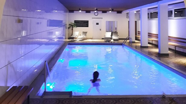 An indoor swimming pool with a tiled floor, benches along the sides, and a ceiling with a wooden panel design. - Centrally located, newly renovated non-smoking apartment with pool and sauna. (Salzburger Land)