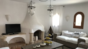 Un salon avec une cheminée, un téléviseur, des meubles en osier et des objets décoratifs disposés sur une table basse.