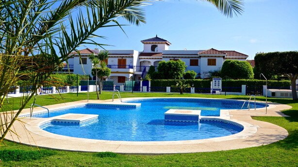 A swimming pool with a circular design, surrounded by a well-maintained lawn and palm trees. - Living room with balcony and sea view, waterfront and south-facing (Vera)