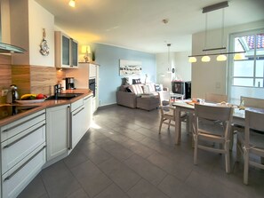 Une cuisine moderne avec des meubles blancs, un plan de travail en bois et un coin repas comprenant une table et des chaises.