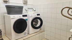 Un espace buanderie équipé de deux machines à laver à chargement frontal, d’un panier et d’un distributeur de lessive.