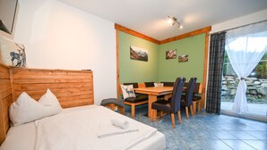 Une chambre à coucher avec un lit, une tête de lit en bois, une table à manger avec des chaises, et une vue sur l’extérieur par une fenêtre.