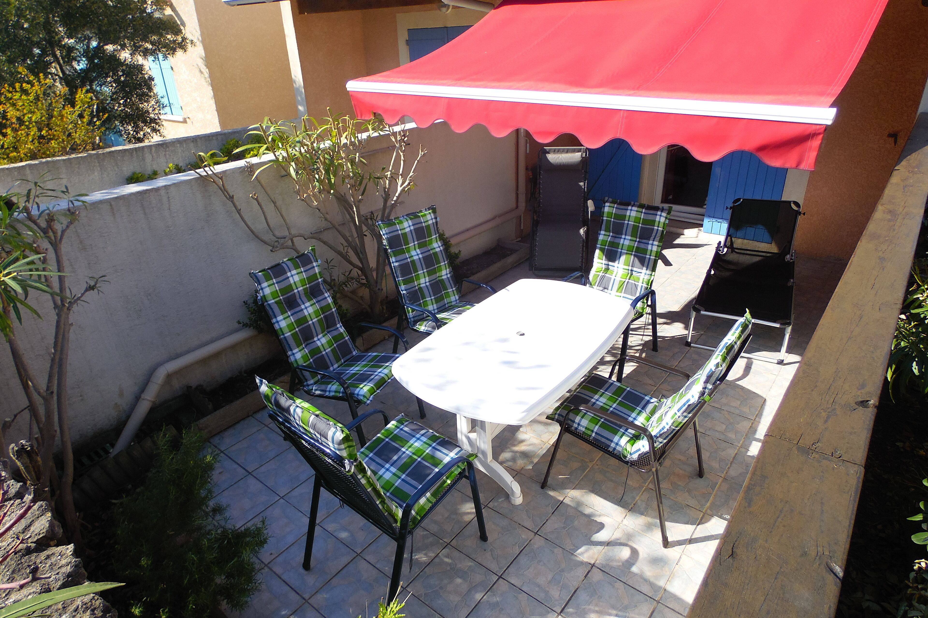 An outdoor patio with a table and chairs, a red canopy, and a view of a building in the background.